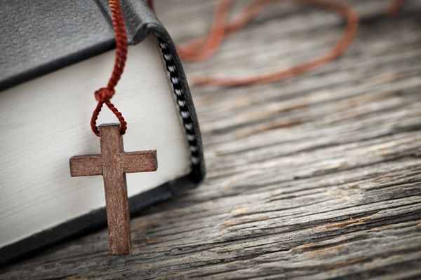 نمای نزدیک از گردن صلیب مسیحی چوبی در کنار کتاب مقدس