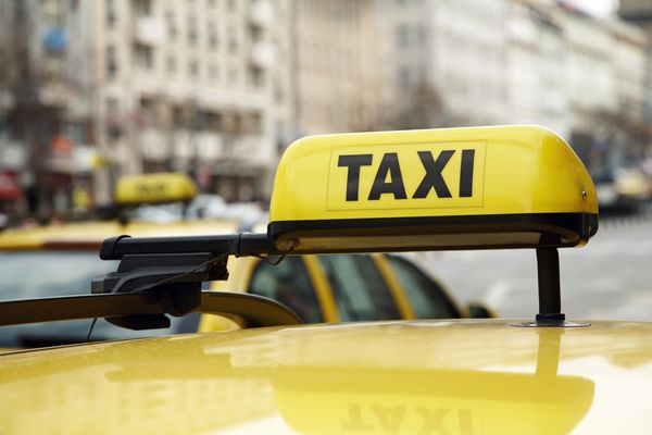 تابلوی تاکسی روی یک ماشین زرد رنگ در خیابان شهری