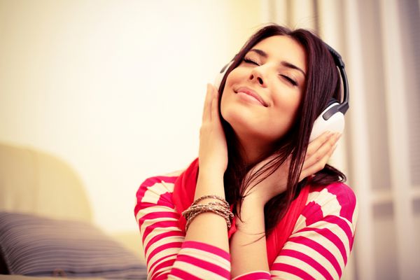 زن جوان زیبا با لباس روشن در حال لذت بردن از موسیقی در خانه