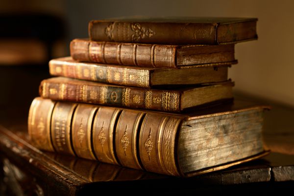 کتاب‌های قدیمی و قدیمی روی موج‌سواری چوبی در نور جهت‌دار گرم انباشته شده‌اند تمرکز انتخابی