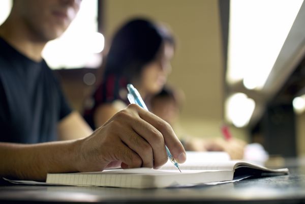 دانشجویان در حال انجام تکالیف و آماده سازی امتحان در دانشگاه نمای نزدیک از مرد جوان که در کتابخانه کالج می نویسد