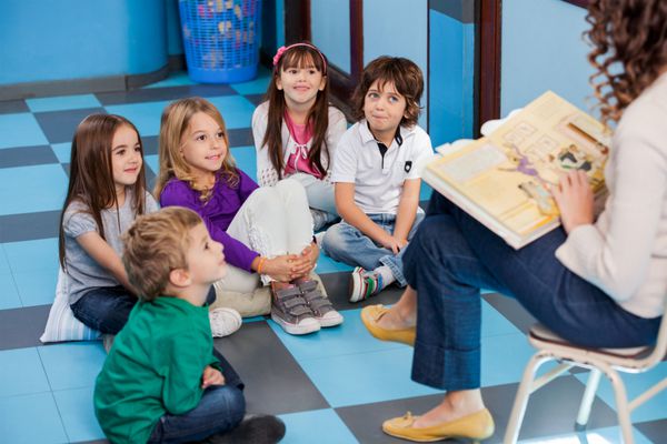 معلم در حال خواندن کتاب داستان برای کودکان در مهدکودک