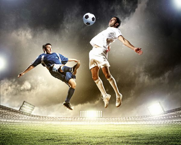 دو بازیکن فوتبال برای ضربه زدن به توپ در ورزشگاه می پرند
