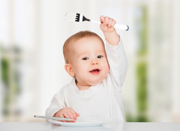 کودک شاد خنده دار با چاقو و چنگال در حال خوردن غذا