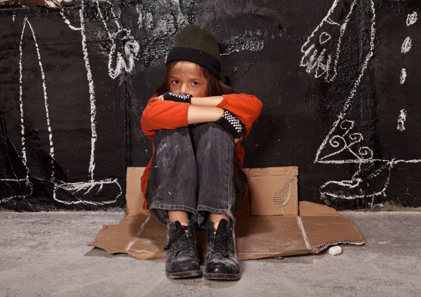 کودک یتیم در مفهوم خیابان - پسری که کنار دیوار با چهره های ترسیم شده والدین نشسته است