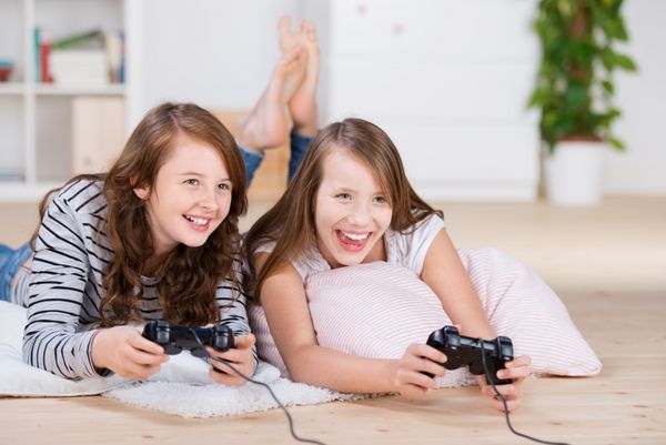 دو دختر جوان با خوشحالی بازی های ویدیویی در کنسولی که روی کف اتاق نشیمن دراز کشیده اند