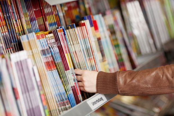 نمای نزدیک از دستان زن در حال انتخاب مجلات از قفسه در سوپرمارکت