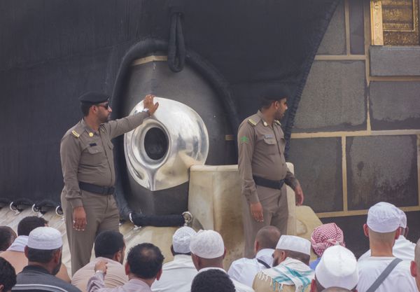 مکه عربستان سعودی - 5 ژوئن مسجد پلیس از سنگ‌های سیاه حجرالاسود که در یک قاب نقره‌ای محصور شده‌اند مراقبت می‌کند مسلمانان معتقدند قدمت سنگ سیاه به زمان حضرت آدم و حوا می‌رسد