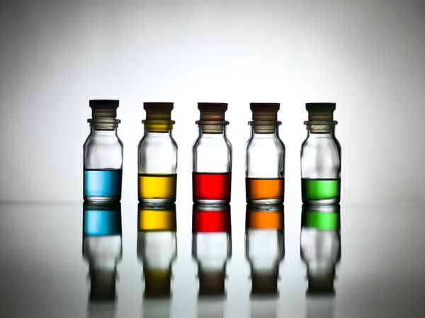 پنج بطری با رنگ های متنوع که روی یک میز منعکس شده است