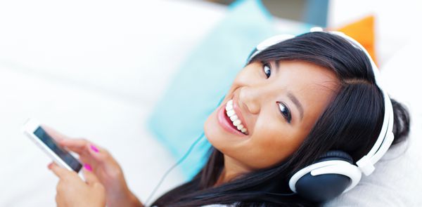 پرتره نزدیک از یک زن جوان آسیایی با هدفون در حال گوش دادن به موسیقی با گوشی هوشمند خود
