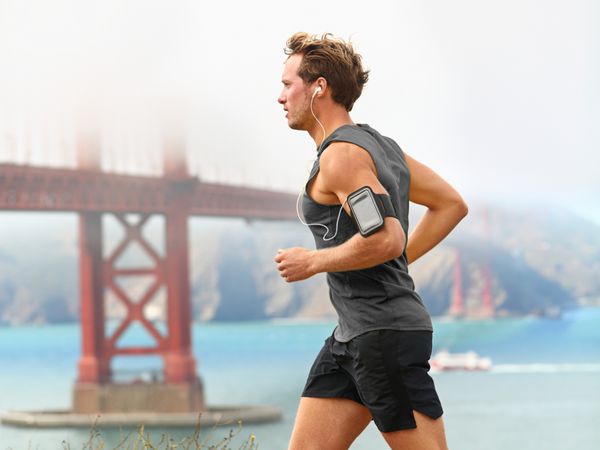 مرد دونده - دونده مرد در سان فرانسیسکو در حال گوش دادن به موسیقی با تلفن هوشمند مرد جوان خوش اندام در حال دویدن در کنار خلیج سان فرانسیسکو و پل گلدن گیت دونده در حال گوش دادن به موسیقی آموزشی در گوشی هوشمند