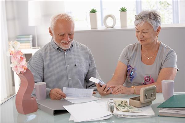 زوج سالمند خوشحال در حال محاسبه بودجه خانواده در خانه