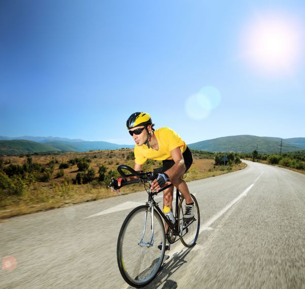 دوچرخه سوار مرد دوچرخه سواری در جاده ای باز در یک روز آفتابی با لنز شیب و شیفت