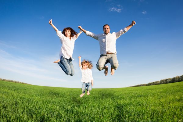 خانواده شاد در حال پریدن در زمین سبز در برابر آسمان آبی مفهوم تعطیلات تابستانی