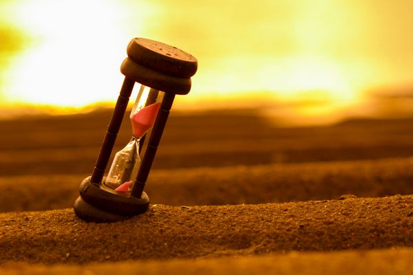نمای نزدیک ساعت شنی روی شن تایمر طلوع آفتاب ساحل