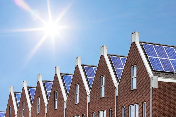 خانه‌های تازه‌ساز با پنل‌های خورشیدی که روی پشت بام و در مقابل آسمان آفتابی وصل شده‌اند
