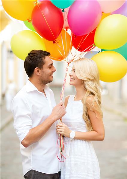 تعطیلات تابستانی جشن و مفهوم دوستیابی - زوج با بالن های رنگارنگ در شهر