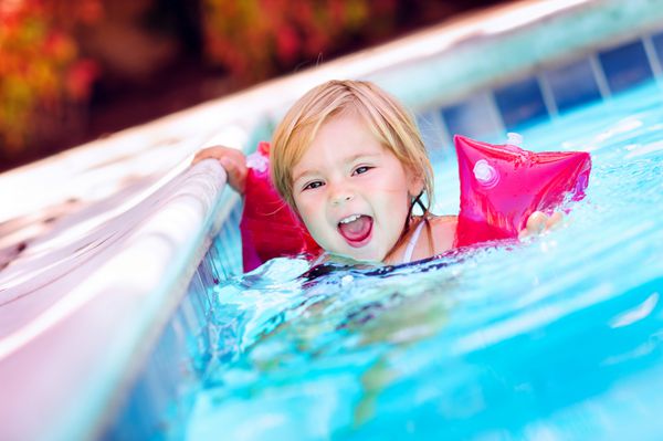 دختر بچه شاد و بامزه ای که با بازوبندهای بادی شنا یاد می گیرد