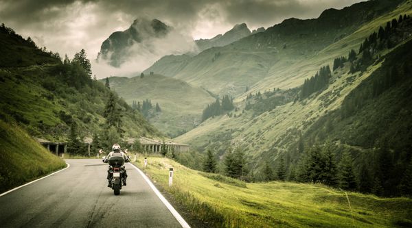 موتورسوار در بزرگراه کوهستانی هوای ابری سرد اروپا اتریش آلپ ورزش شدید سبک زندگی فعال مفهوم تور ماجراجویی