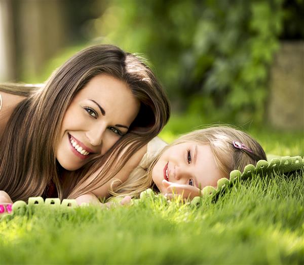 زن جوان زیبا با یک دختر در چمنزار در باغ