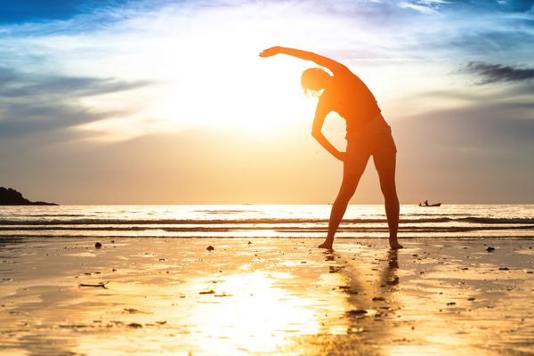 شبح زن جوان ورزش در ساحل در غروب آفتاب