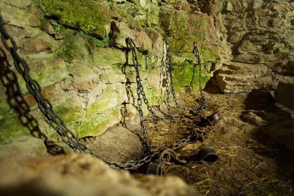زندان سیاه چال قلعه با زنجیر زنجیر و خزه روی دیوارهای سنگی