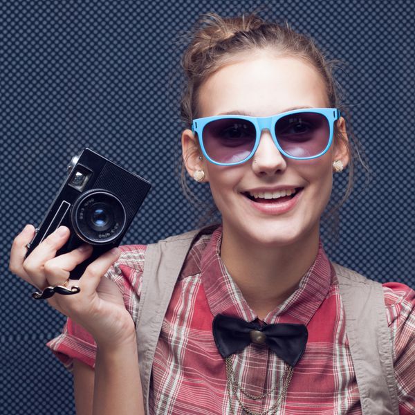 دختر هیپستر خندان با دوربین قدیمی نوجوان مد روز با پیراهن قرمز چهارخانه و پاپیون و عینک آفتابی