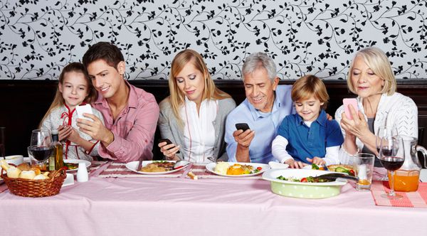 خانواده ای که پشت میز شام به گوشی های هوشمند خود نگاه می کنند