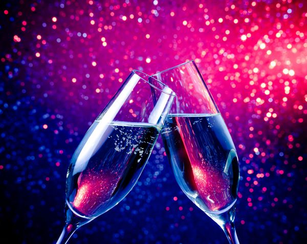 یک جفت فلوت شامپاین با حباب‌ها روی پس‌زمینه بوکه روشن با رنگ آبی شادی می‌کنند