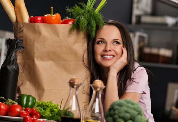 زن جوان با کیسه مواد غذایی پر از سبزیجات تازه در آشپزخانه مدرن