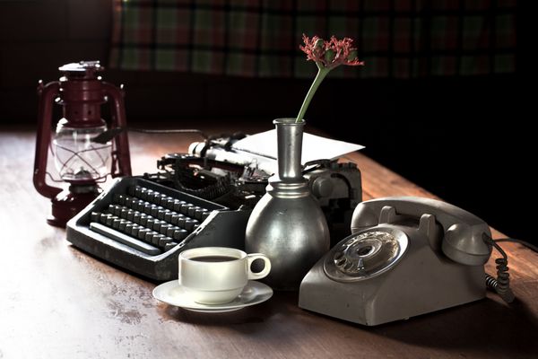 طبیعت بی جان دفتر رترو تلفن تایپ نویس و گل در گلدان نقره ای pl نزدیک چراغ قدیمی روی میز چوبی