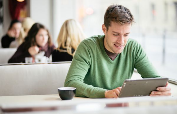 دانشجوی جوان با استفاده از رایانه لوحی در کافه