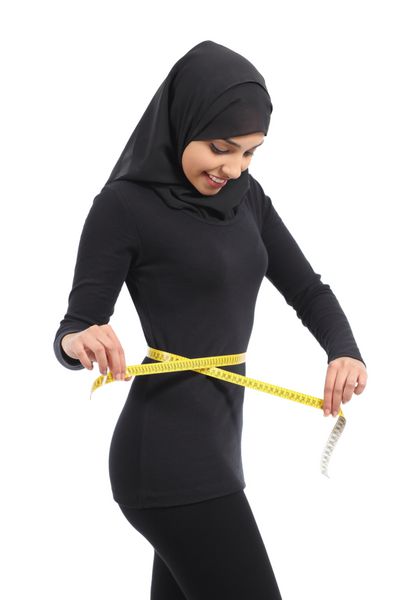 زن عرب در حال اندازه گیری دور کمر با نوار اندازه گیری پس زمینه سفید را جدا می کند