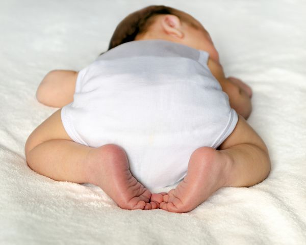 نوزادی که روی سفید می خوابد نمای عقب باسن در پوشک با پاها و پاهای ضربدری شایان ستایش