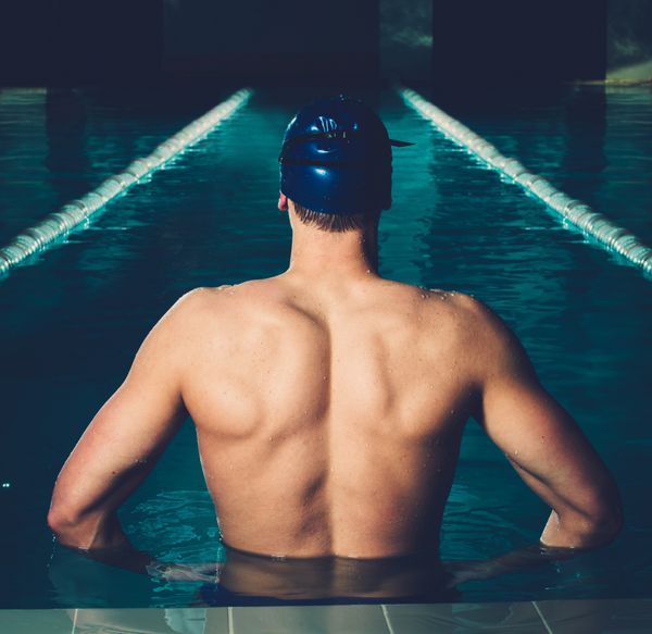 مرد جوان عضلانی با کلاه آبی در استخر شنا