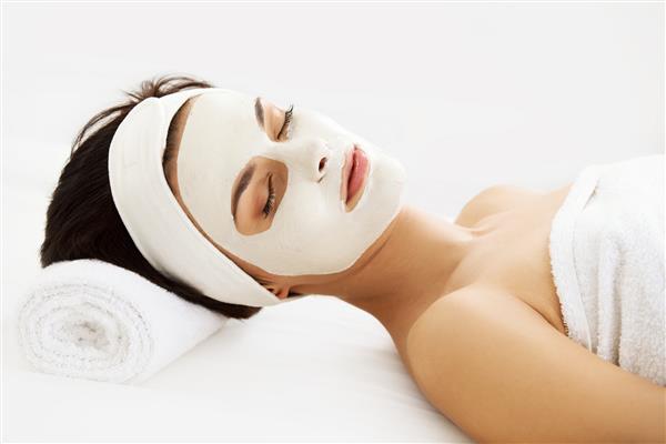 ماسک آرایشی زن جوان زیبا در حال درمان زیبایی در سالن اسپا جدا شده روی زمینه سفید