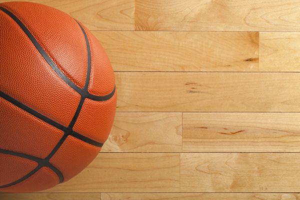 یک توپ بسکتبال روی یک زمین ورزشگاه چوبی که از بالا مشاهده می شود