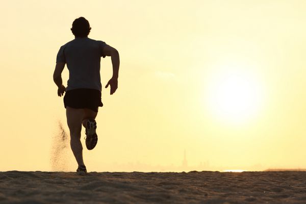 نمای پشتی مرد دونده ای که در غروب آفتاب در ساحل می دود و خورشید در پس زمینه