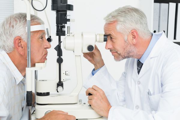 نمای جانبی اپتومتریست در حال انجام تست بینایی برای بیمار مسن