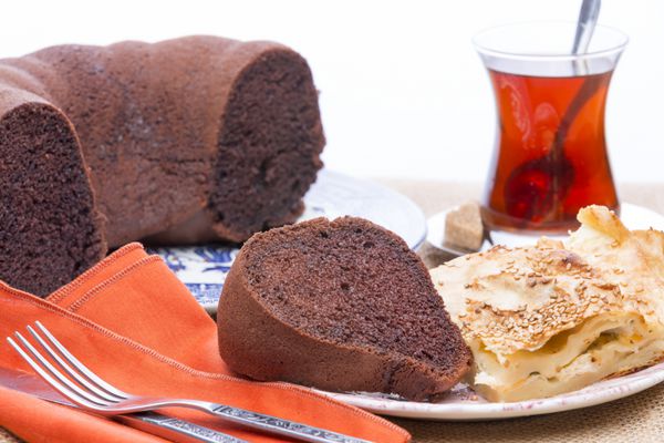 نمای پایین برش های بورک تازه پخته شده و کیک شکلاتی که در یک بشقاب در یک مهمانی با یک لیوان چای سنتی ترکیه سرو می شود