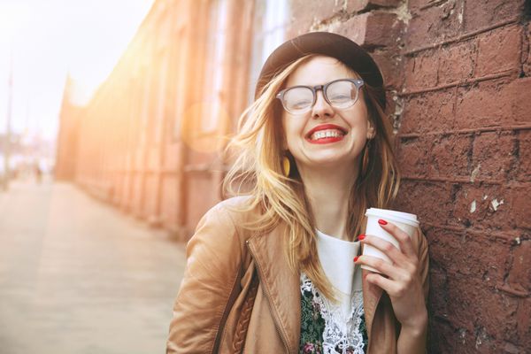 زن شاد در خیابان در حال نوشیدن قهوه صبح در نور آفتاب