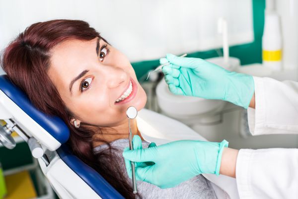 زن خندان در دندانپزشک نشسته روی صندلی دندانپزشکی آماده برای معاینه دندانپزشکی است