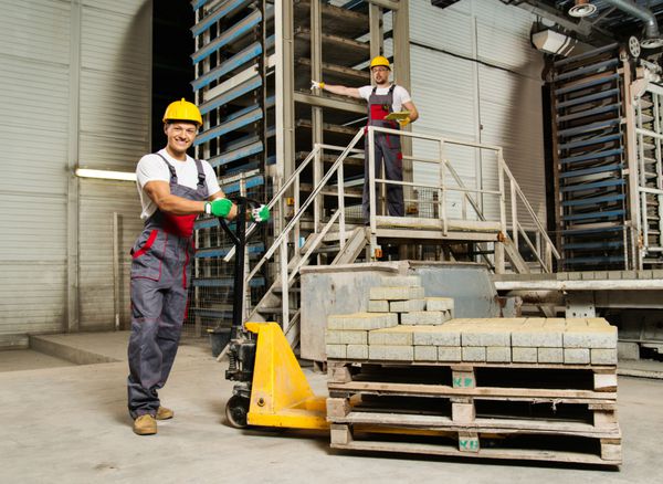 کارگر جوان سنگ‌فرش را با پالت‌کامیون روی یک کارخانه جابجا می‌کند