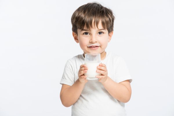 پسر بچه شایان ستایش با شیر نوشیدنی با سبیل شیری که لیوان شیر در دست دارد