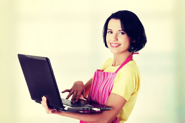 خانه دار مدرن یا کارگر زن با لپ تاپ که پیش بند صورتی پوشیده است