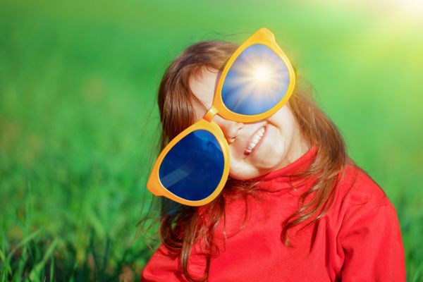 دختر کوچک شاد با عینک آفتابی بزرگ در چمنزار