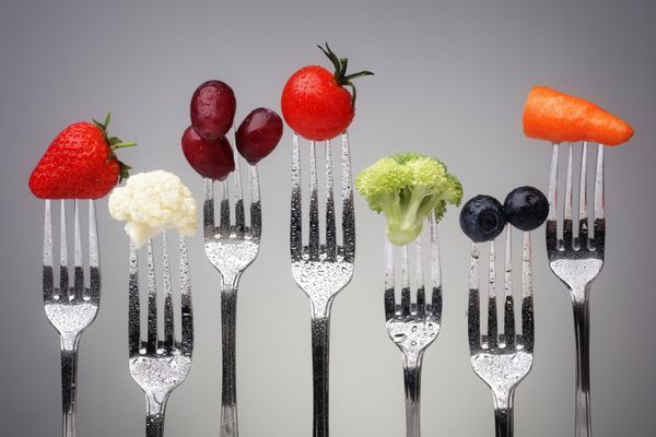 میوه و سبزیجات چنگال های نقره ای در برابر مفهوم پس زمینه خاکستری برای تغذیه سالم رژیم غذایی و آنتی اکسیدان