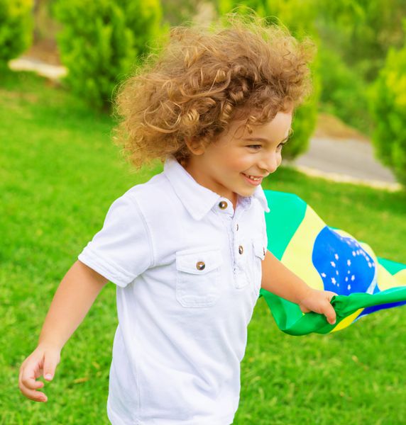 پرتره پسر کوچک ناز در حال دویدن با پرچم ملی برزیل فوتبالیست جوان شاد هوادار تیم فوتبال برزیل