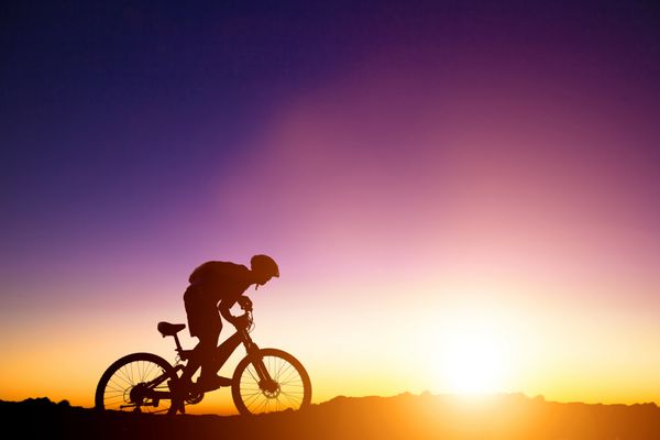 دوچرخه سوار کوهستانی روی تپه با پس زمینه طلوع خورشید