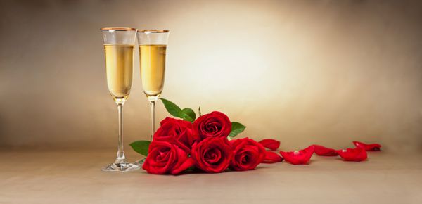 لیوان شامپاین هدیه و گل رز در مقابل پس زمینه بژ
